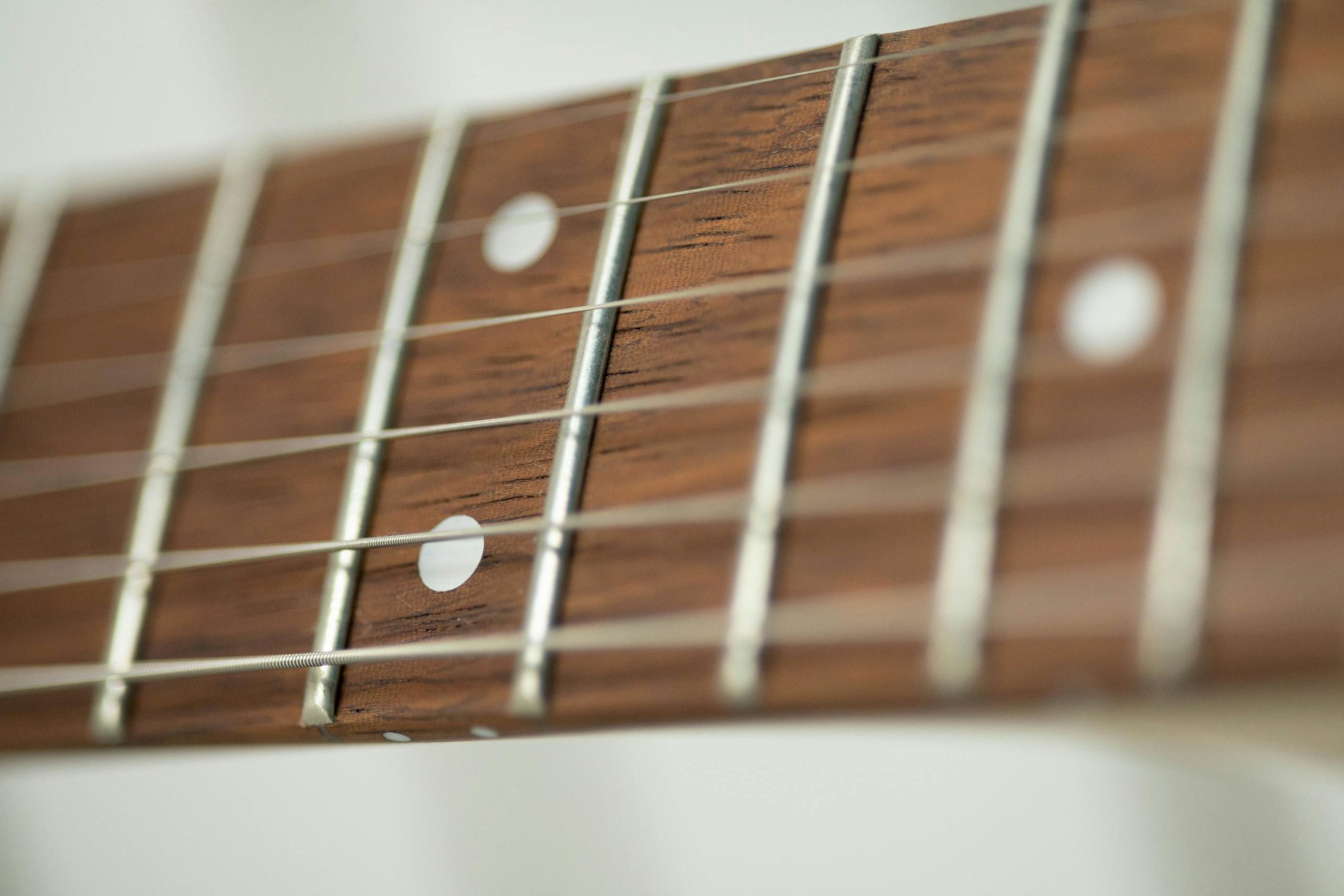 Detailed vertical close-up of a guitar fretboard showing strings and inlays.