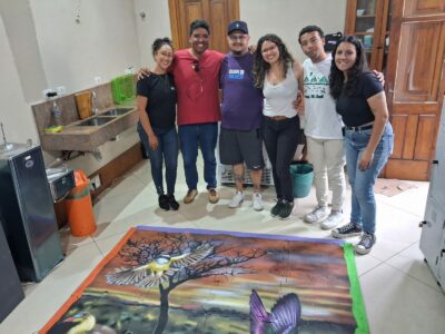 Na parte interna do museu, da esquerda para a direita, Kétellin, Leandro, Anderson, Lisiane, Hiago e Maria Luiza estão, lado a lado, abraçados e sorridentes diante do quebra-cabeça montado no chão.