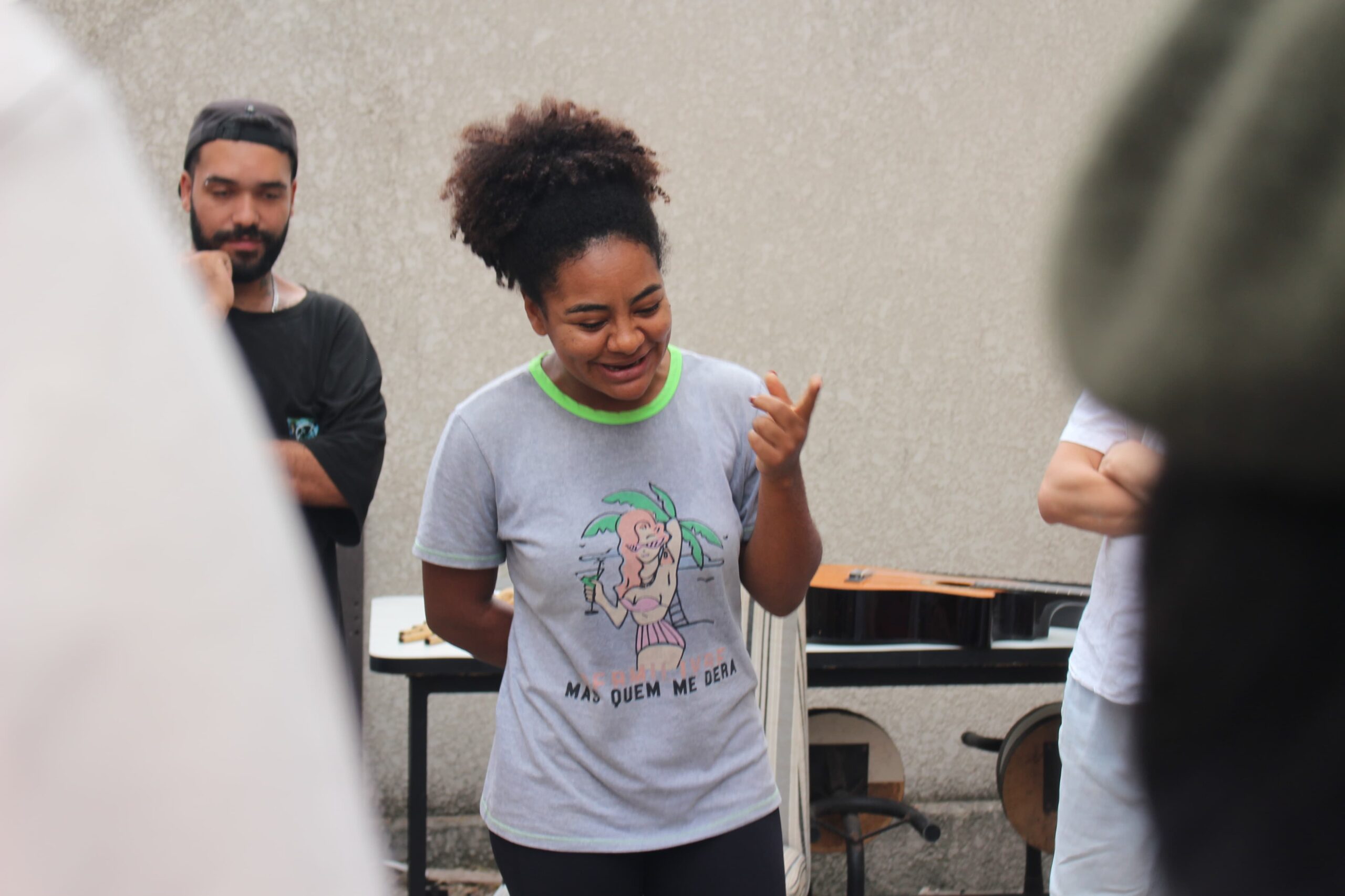 Tainara, estudante quilombola e mulher negra, veste uma camiseta cinza e olha para baixo com expressão alegre